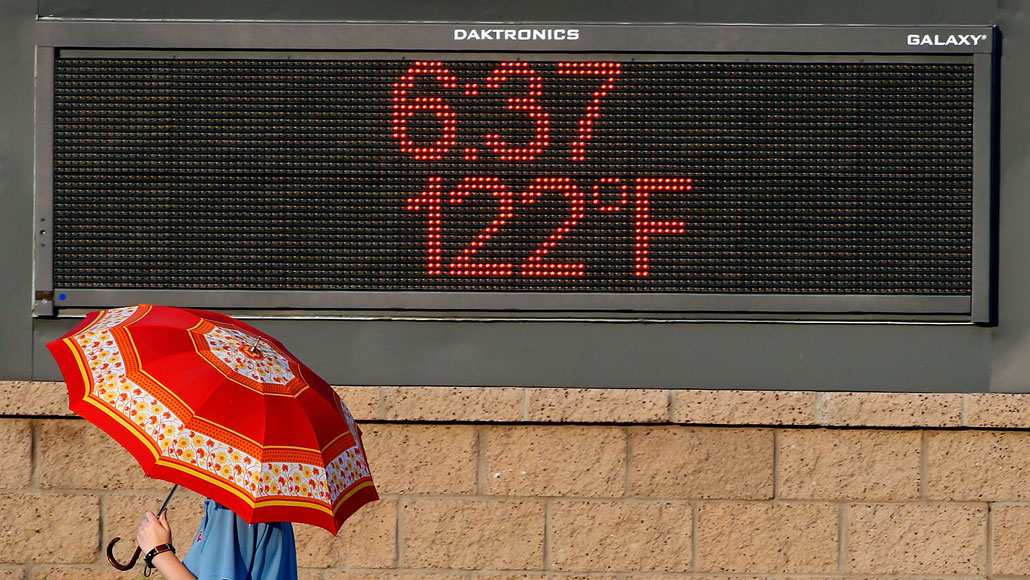 persoon die langs een elektronisch bord in Phoenix loopt met de tekst 122 graden en 18:27 uur