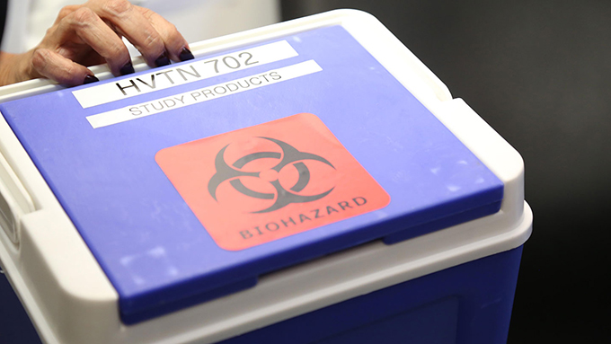 a hand holding the handle of a small blue cooler with a red 'biohazard' sticker on it