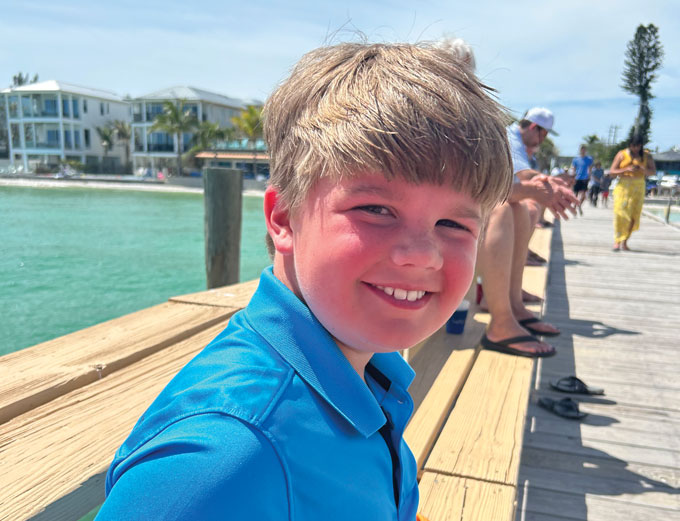 Will Ungerer sits on a pier with water and houses in the background. He's smiling.